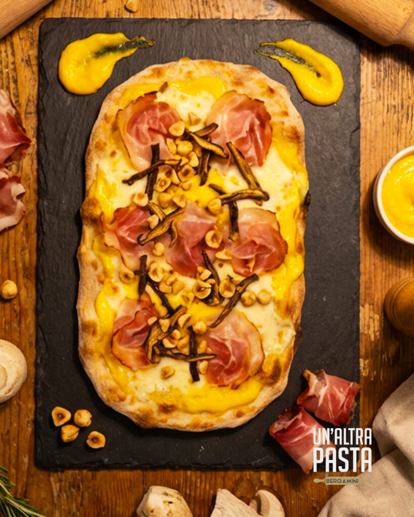 In occasione delle Olimpiadi Invernali Milano-Cortina 2026, Un’Altra Pasta celebra lo spirito sportivo italiano con una creazione inedita: la Pinsa “Milano-Cortina”. Una base bianca con sola mozzarella, avvolta da una crema di zafferano (panna, mascarpone e zafferano), impreziosita da speck, porcini e granella di nocciole. Un mix di sapori che racconta l’incontro tra tradizione e gusto contemporaneo.